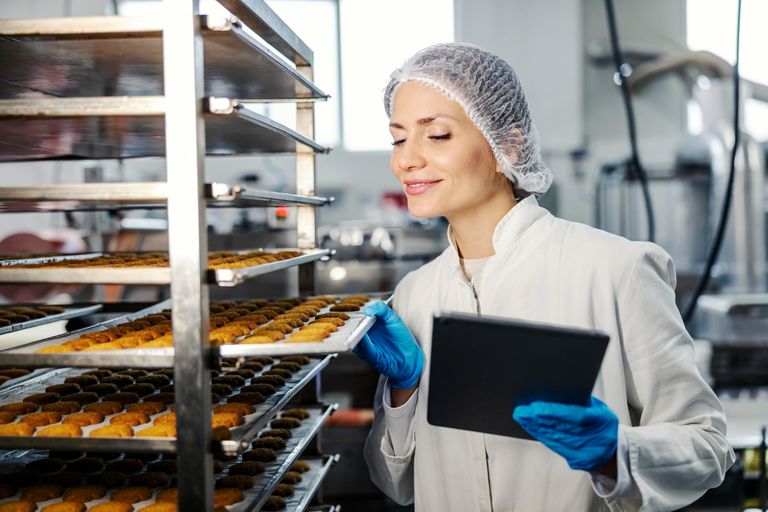 Trabajador de panadería industrial realizando inspección de calidad con tableta digital en línea de producción